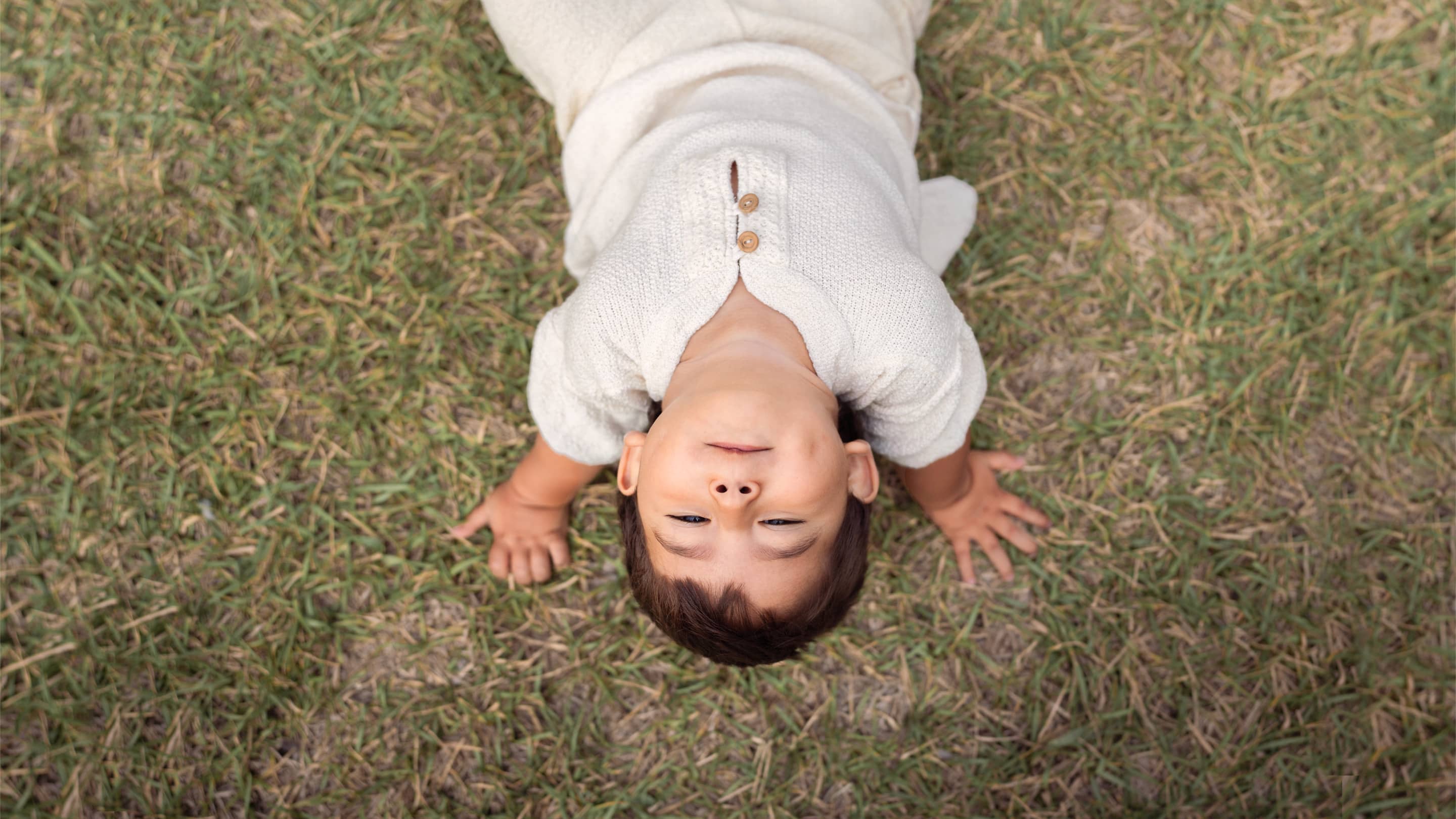 Little boy sitting in grass, wearing Tanguis cotton shirt with wooden buttons and Tanguis cotton shorts by Liten Aventuris. | Liten pojke sitter i gräset, iförd Tanguis bomullsskorta med träknappar och Tanguis-bomullsbyxor från Liten Aventuris. | Niño pequeño sentado en el césped, vistiendo camisa de algodón Tanguis con botones de madera y shorts de algodón tanguis de Liten Aventuris.
