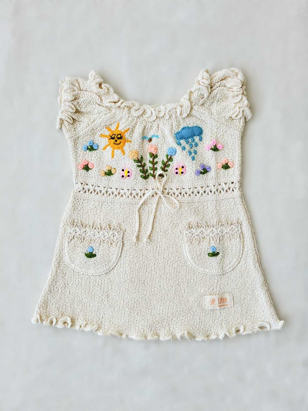 Liten Aventuris Collections. Let your little one shine like the sun in our Sol Dress! Perfect for summer days with its puffed sleeves, wavy edges, two pockets, and colorful hand-embroidered elements inspired by nature, farm animals, and – of course – the happy sun! The Sol dress is made of natural knitted Tanguis cotton. This dress is a comfy, stylish pick for your little explorer! Ethically made in Peru. Ekologisk klänning för flickor och bebisar.