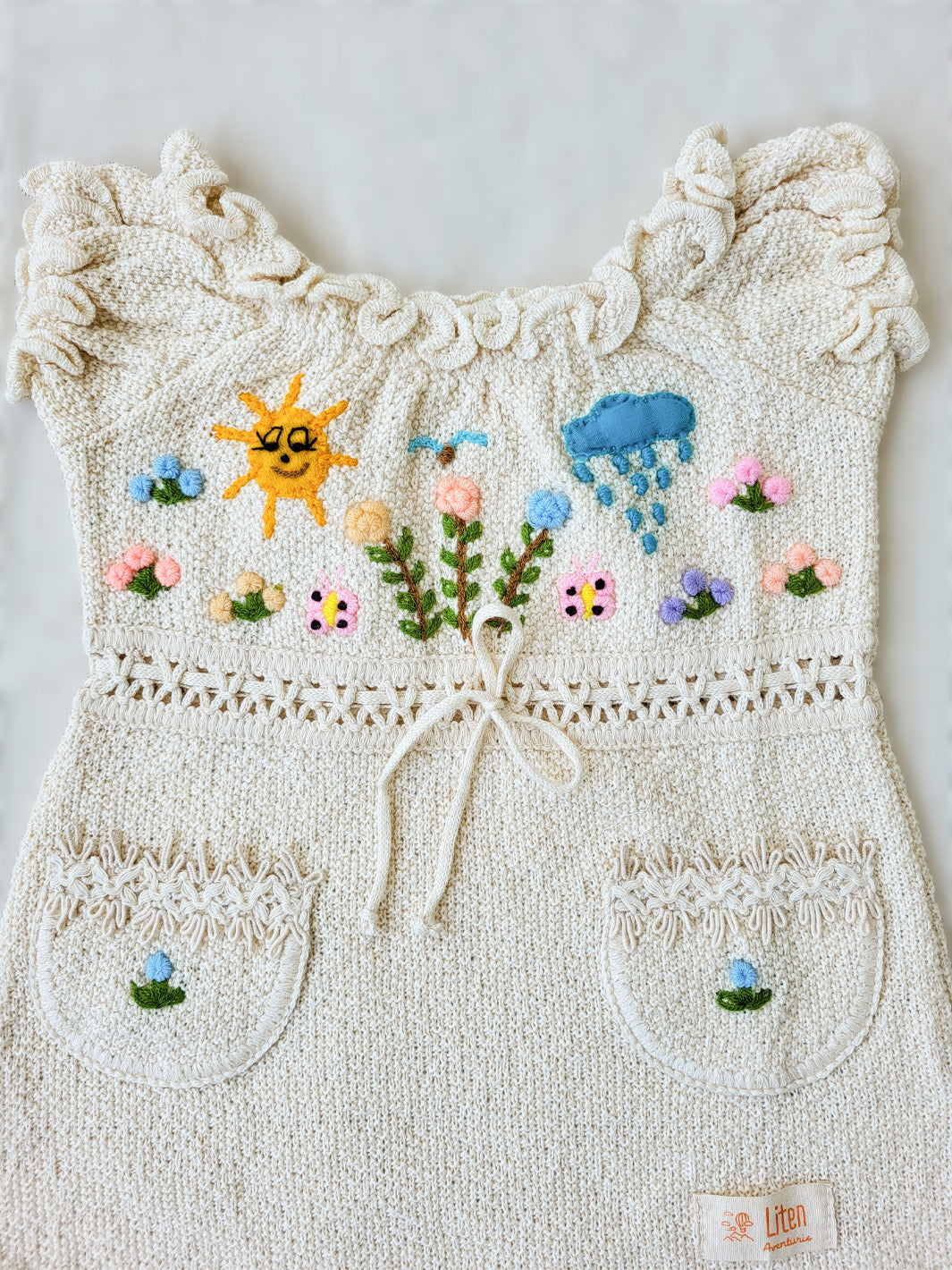 Liten Aventuris Collections. Let your little one shine like the sun in our Sol Dress! Perfect for summer days with its puffed sleeves, wavy edges, two pockets, and colorful hand-embroidered elements inspired by nature, farm animals, and – of course – the happy sun! The Sol dress is made of natural knitted Tanguis cotton. This dress is a comfy, stylish pick for your little explorer! Ethically made in Peru. Ekologisk klänning för flickor och bebisar.
