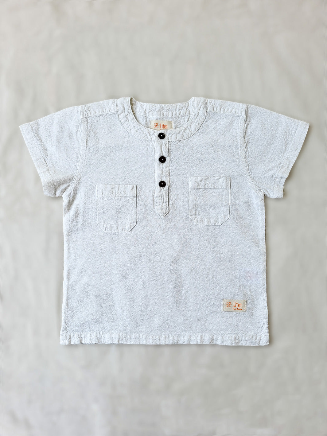 Liten Aventuris Natural Tocuyo Cotton shirt for kids. The Philipo shirt is perfect for a picnic at a lake or a nice morning stroll! This short sleeve shirt with coconut buttons and tunisian collar is casual and chic at the same time. This loose-fitting shirt with two pockets, is comfortable and soft with the skin. Ethically made in Peru. Bomullskläder, barnkläder, Pojken tröja, Natural kläder, ekologisk kläder. Skjortor.