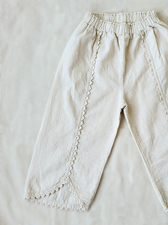 Liten Aventuris Natural Tocuyo Cotton pants for kids. Our Lorin pants are perfect for sunny days. With its loose-fitting size and soft elastic on the waist, toddlers and kids will feel comfortable and free. The Lorin pants bring an embroidered cotton decorative ribbon that will be the perfect match to our Lorin T-shirt! Perfect for girls. Barnkläder, Bomullskläder, Natural kläder. Flicka kläder. Barn Byxor.