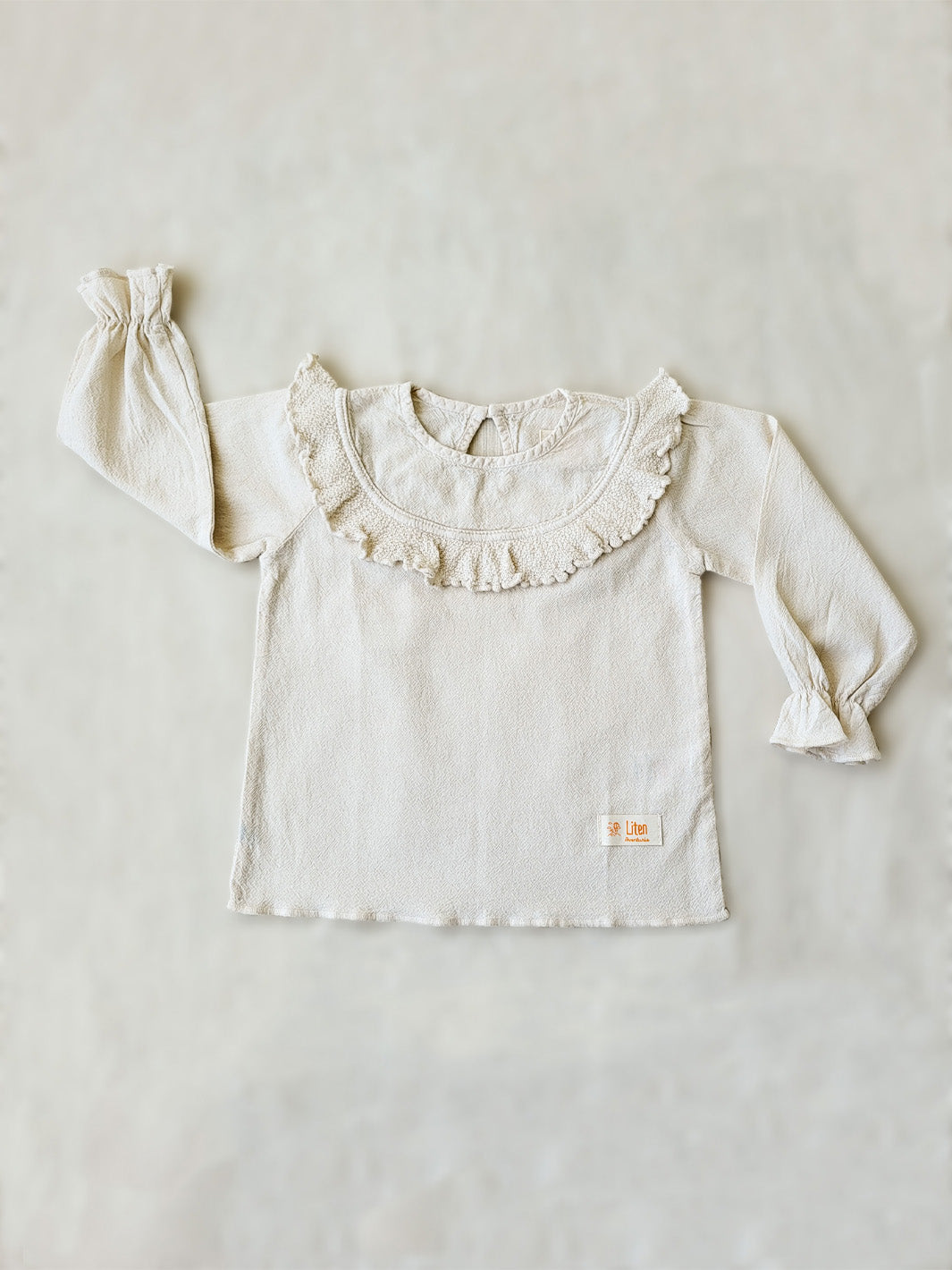 Liten Aventuris. Our Siri Blouse is elegant and comfortable at the same time. Its long sleeves with ruffles on the wrists are perfect for an evening stroll. The knitted cotton ruffles on the chest add a nice artisanal touch. Part of our Collection. Loose-fitting garment. 100% Flat-knitted Natural Peruvian Tocuyo Cotton. 100% knitted Natural Tanguis Cotton. Ethically made in Peru. Perfect for girls. Barnkläder, Bomullskläder, Natural kläder. Flicka kläder. Flickblus. Barnblus.