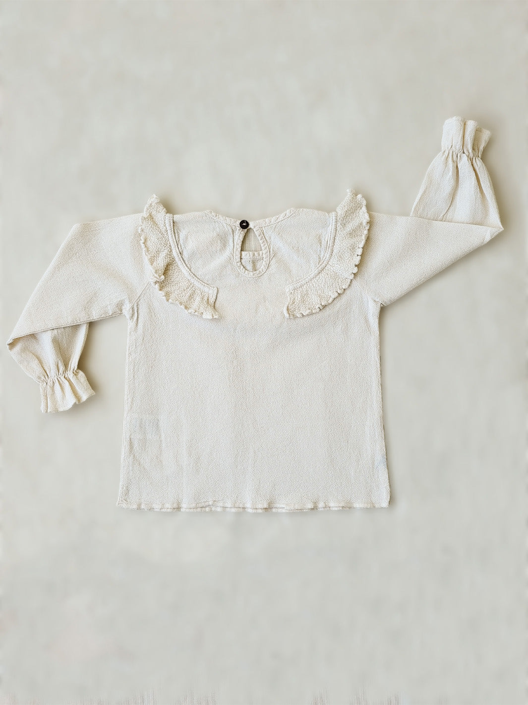 Liten Aventuris. Our Siri Blouse is elegant and comfortable at the same time. Its long sleeves with ruffles on the wrists are perfect for an evening stroll. The knitted cotton ruffles on the chest add a nice artisanal touch. Part of our Collection. Loose-fitting garment. 100% Flat-knitted Natural Peruvian Tocuyo Cotton. 100% knitted Natural Tanguis Cotton. Ethically made in Peru. Perfect for girls. Barnkläder, Bomullskläder, Natural kläder. Flicka kläder. Flickblus. Barnblus.