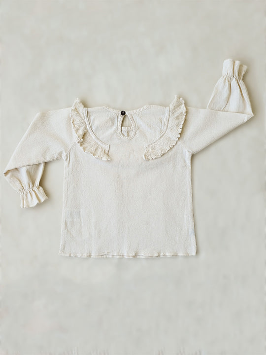 Liten Aventuris. Our Siri Blouse is elegant and comfortable at the same time. Its long sleeves with ruffles on the wrists are perfect for an evening stroll. The knitted cotton ruffles on the chest add a nice artisanal touch. Part of our Collection. Loose-fitting garment. 100% Flat-knitted Natural Peruvian Tocuyo Cotton. 100% knitted Natural Tanguis Cotton. Ethically made in Peru. Perfect for girls. Barnkläder, Bomullskläder, Natural kläder. Flicka kläder. Flickblus. Barnblus.