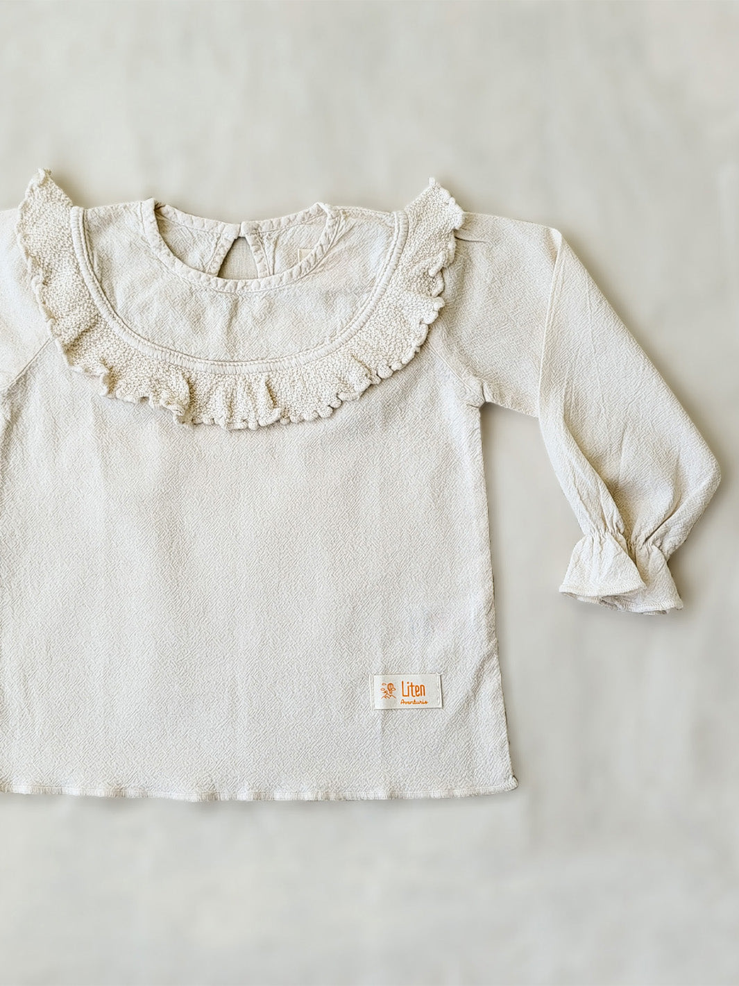 Liten Aventuris. Our Siri Blouse is elegant and comfortable at the same time. Its long sleeves with ruffles on the wrists are perfect for an evening stroll. The knitted cotton ruffles on the chest add a nice artisanal touch. Part of our Collection. Loose-fitting garment. 100% Flat-knitted Natural Peruvian Tocuyo Cotton. 100% knitted Natural Tanguis Cotton. Ethically made in Peru. Perfect for girls. Barnkläder, Bomullskläder, Natural kläder. Flicka kläder. Flickblus. Barnblus.
