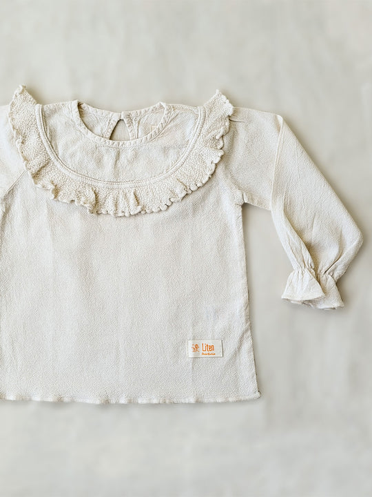 Liten Aventuris. Our Siri Blouse is elegant and comfortable at the same time. Its long sleeves with ruffles on the wrists are perfect for an evening stroll. The knitted cotton ruffles on the chest add a nice artisanal touch. Part of our Collection. Loose-fitting garment. 100% Flat-knitted Natural Peruvian Tocuyo Cotton. 100% knitted Natural Tanguis Cotton. Ethically made in Peru. Perfect for girls. Barnkläder, Bomullskläder, Natural kläder. Flicka kläder. Flickblus. Barnblus.