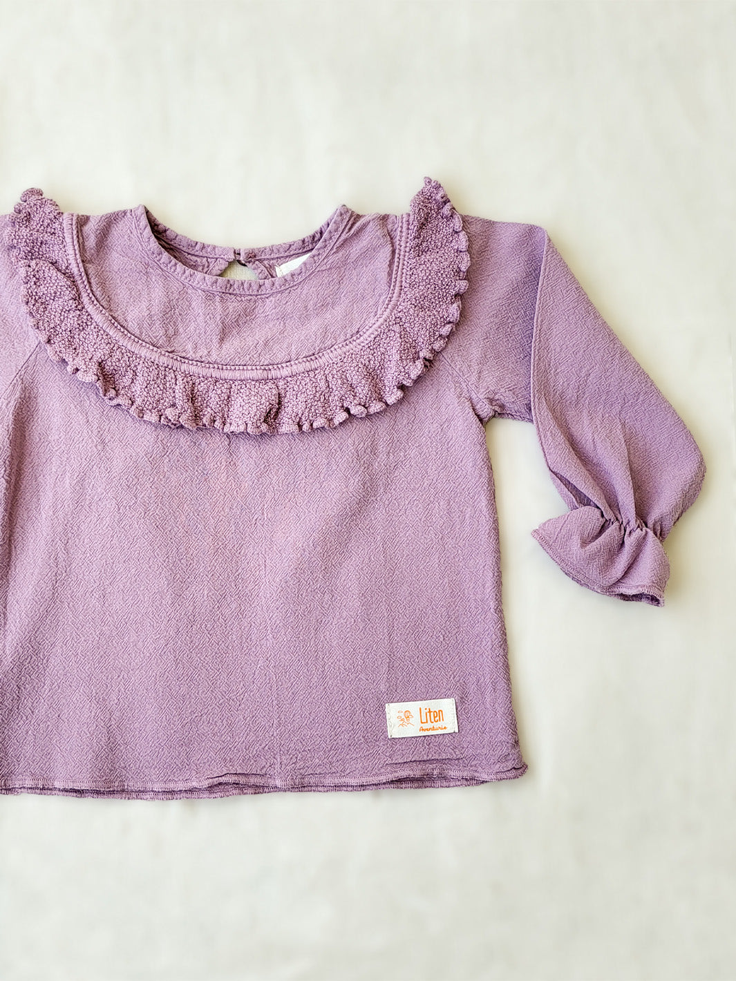 Liten Aventuris. Our Siri Blouse is elegant and comfortable at the same time. Its long sleeves with ruffles on the wrists are perfect for an evening stroll. The knitted cotton ruffles on the chest add a nice artisanal touch. Part of our Collection. Loose-fitting garment. 100% Flat-knitted Natural Peruvian Tocuyo Cotton. 100% knitted Natural Tanguis Cotton. Ethically made in Peru. Perfect for girls. Barnkläder, Bomullskläder, Natural kläder. Flicka kläder. Flickblus. Barnblus.