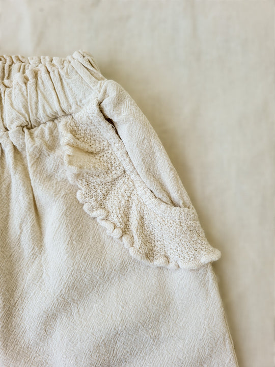The Siri Pants are elegant and comfortable at the same time. These bloomer pants with ruffles at the bottom are perfect for a walk on the beach or a nice play date at the park. The Siri Pants bring two pockets with knitted cotton ruffles on them. It adds a nice artisanal touch. Beautiful, chic, and charming! Make the perfect match with the Siri blouse. 100% Natural Peruvian Tocuyo Cotton. Perfect for girls. Barnkläder, Bomullskläder, Natural kläder. Flicka kläder. Barn Byxor.