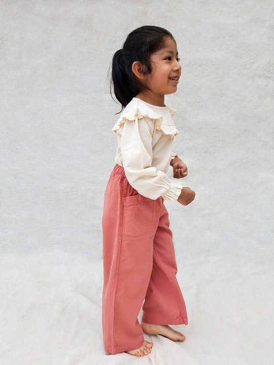 Liten Aventuris. Our Siri Blouse is elegant and comfortable at the same time. Its long sleeves with ruffles on the wrists are perfect for an evening stroll. The knitted cotton ruffles on the chest add a nice artisanal touch. Part of our Collection. Loose-fitting garment. 100% Flat-knitted Natural Peruvian Tocuyo Cotton. 100% knitted Natural Tanguis Cotton. Ethically made in Peru. Perfect for girls. Barnkläder, Bomullskläder, Natural kläder. Flicka kläder. Flickblus. Barnblus.