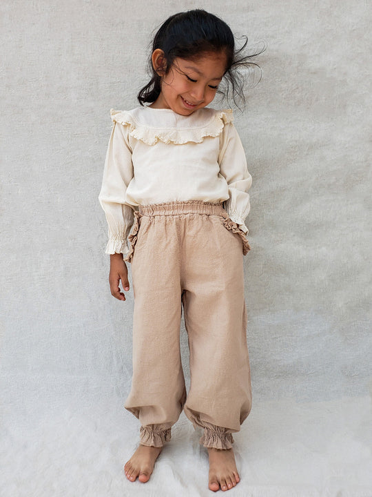 The Siri Pants are elegant and comfortable at the same time. These bloomer pants with ruffles at the bottom are perfect for a walk on the beach or a nice play date at the park. The Siri Pants bring two pockets with knitted cotton ruffles on them. It adds a nice artisanal touch. Beautiful, chic, and charming!  Make the perfect match with the Siri blouse. 100% Natural Peruvian Tocuyo Cotton. Perfect for girls. Barnkläder, Bomullskläder, Natural kläder. Flicka kläder. Barn Byxor.